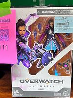 Front view of sealed box showing Sombra figure, accessories, branding and price sticker