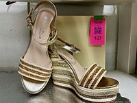 Side and top view of both sandals showing gold metallic finish, braided platform and ankle strap