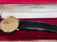 Watch in open Omega box showing gold dial and black strap