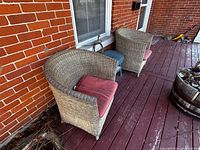 Two wicker armchairs with cushions beside blue wicker table on porch