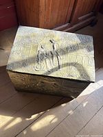 Closed brass-clad box showing embossed lid scene