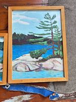 larger framed painting depicting lake, rock outcrop, pine tree