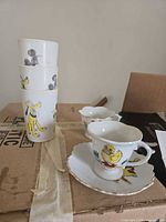 Stacked Disney plastic cups, porcelain teacups and saucer on box