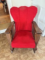 Front view of antique wooden rocking chair, showing red wingback upholstery and slatted arms