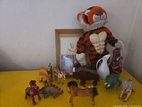 Full lot with all figurines, plush tiger, pitcher, framed print and decorative bottle displayed on yellow surface