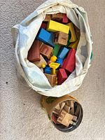 Fabric tote full of various painted wooden blocks beside cardboard canister of alphabet blocks