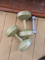 Three dumbbells: two light green vinyl-coated round-end, one grey cast iron hex
