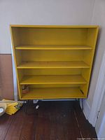 Front view of yellow wooden bookshelf with four shelves and metal hairpin legs