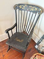 Front angle view of painted wooden rocking chair showing floral decoration, spindle back and wear