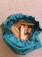 Open teal drawstring bag filled with assorted wooden train track pieces