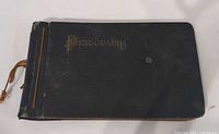 Front cover showing black cloth boards, gold title, string binding, spine damage