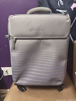 Front view of IT Luggage carry-on spinner showing exterior color, stripes, wheels, and front pocket