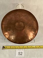 Full back view showing hammered copper surface, hanging loops, diameter reference with tape