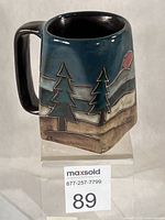 Front view showing etched forest scene and red sun on teal glaze mug