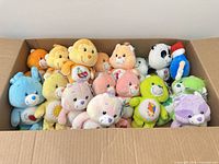 Box filled with Care Bear plush toys, panda plush and blue plush with red hat