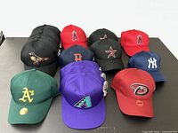 Sixteen MLB caps arranged in rows on black surface; various team logos visible front view