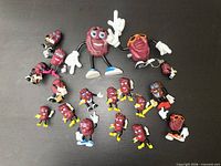 Full group of 18 California Raisins figurines on black surface