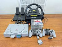 Overall lot showing PS1 console, controllers, steering wheel, pedals, memory cards, stack of game cases