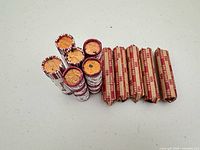 Overview of thirteen wrapped penny rolls: six white/red striped standing vertically and seven brown "50¢ Pennies" rolls lying horizontally