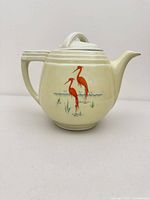 Front view of cream ceramic coffee pot with red herons and lid attached