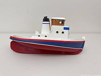 Side profile of painted wooden toy tugboat showing hull, cabin and smokestack