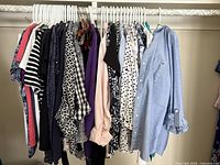 Rack of approximately 24 women’s tops on white plastic hangers