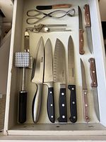 Drawer with meat mallet, four large knives, three steak knives, garlic press, tongs and citrus zester