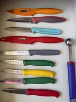 Top-down view of eight coloured-handle knives and one melon baller on cutting board