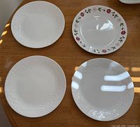 Four dinner plates on table: three embossed white, one floral rim