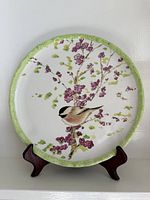 Front view of ceramic plate on stand showing bird and blossom design and green rim
