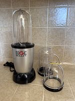 Overall view of blender base with tall cup attached and two extra cups beside