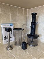 Front view of immersion blender handle, blending shaft, whisk, blending cup, chopper bowl, and user guide