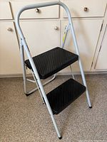Full view of gray two-step folding ladder with black steps