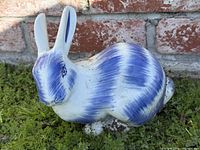 Left-side view of blue and white ceramic bunny on grass against brick wall