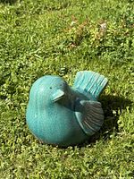 Front angle of turquoise ceramic bird sculpture on grass