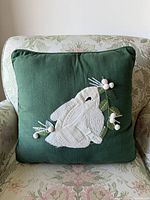 Full view of green pillow with bunny appliqué on patterned armchair