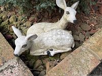 Pair of reclining fawn statues in garden bed