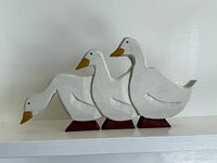 Three white hand-carved wooden geese on red bases