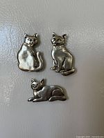 Front view of three pewter cat magnets on refrigerator surface