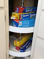 Two-tier cabinet lazy Susan holding boxed wax paper, plastic wrap, aluminum foil and storage bags