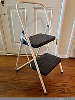 Overall view of white frame two-step folding ladder with black steps