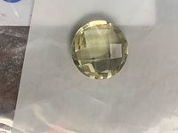 Round pale green gemstone on plastic sleeve showing checkerboard facets