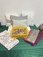 Overall lot: pillows, basket of clothespins, folded fabrics displayed on table