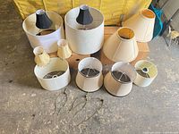 Assorted lamp shades and harps spread on floor showing variety in size and color