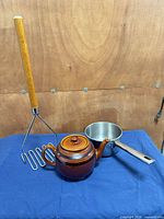 Group shot of brown teapot, Lagostina saucepan, wood-handled potato masher