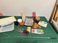Overall lot layout on table showing mixer, bake pan, cups, trays, containers, skewers, molds, wooden plaque