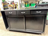 front view of black wood sideboard showing three drawers, two pegboard sliding doors and overall condition