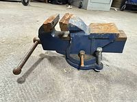 side view of blue cast iron bench vise on swivel base with handle and mounting bolt