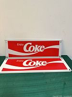 Front view of both Coca-Cola "Enjoy Coke" metal signs showing graphics and condition