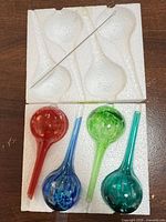 Four glass watering globes stored in molded foam tray with cleaning brush visible